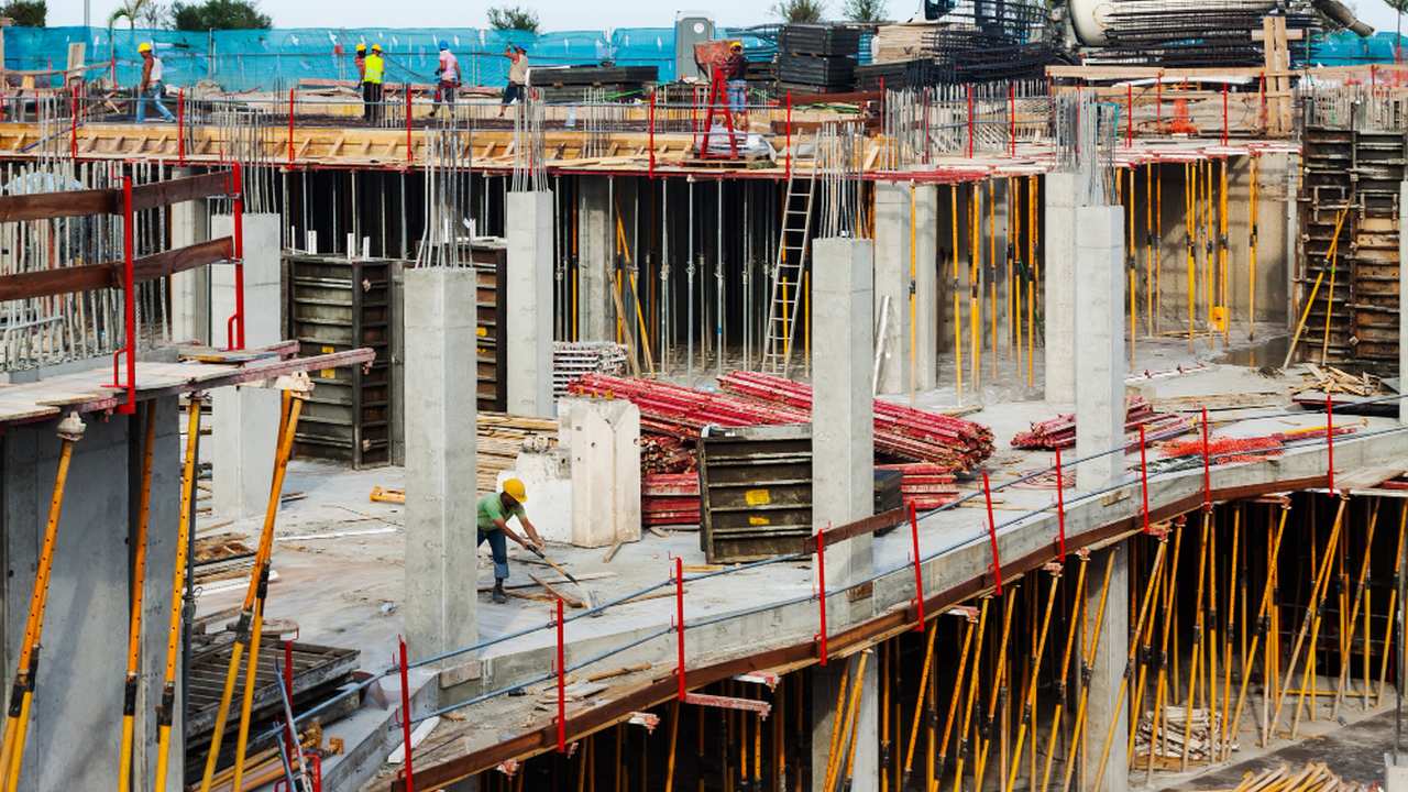 Construção em andamento em Nova Friburgo, com trabalhadores e estruturas de concreto e madeira.