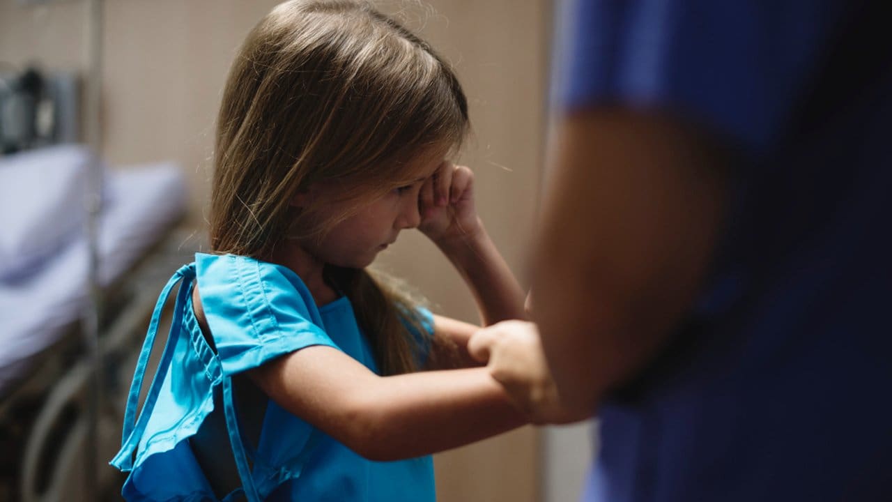 Criança em hospital com expressão de preocupação, possivelmente devido à falta de médicos.
