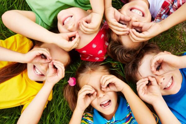 Crianças felizes brincando na grama, com as mãos nos olhos, simbolizando a infância e a inocência.