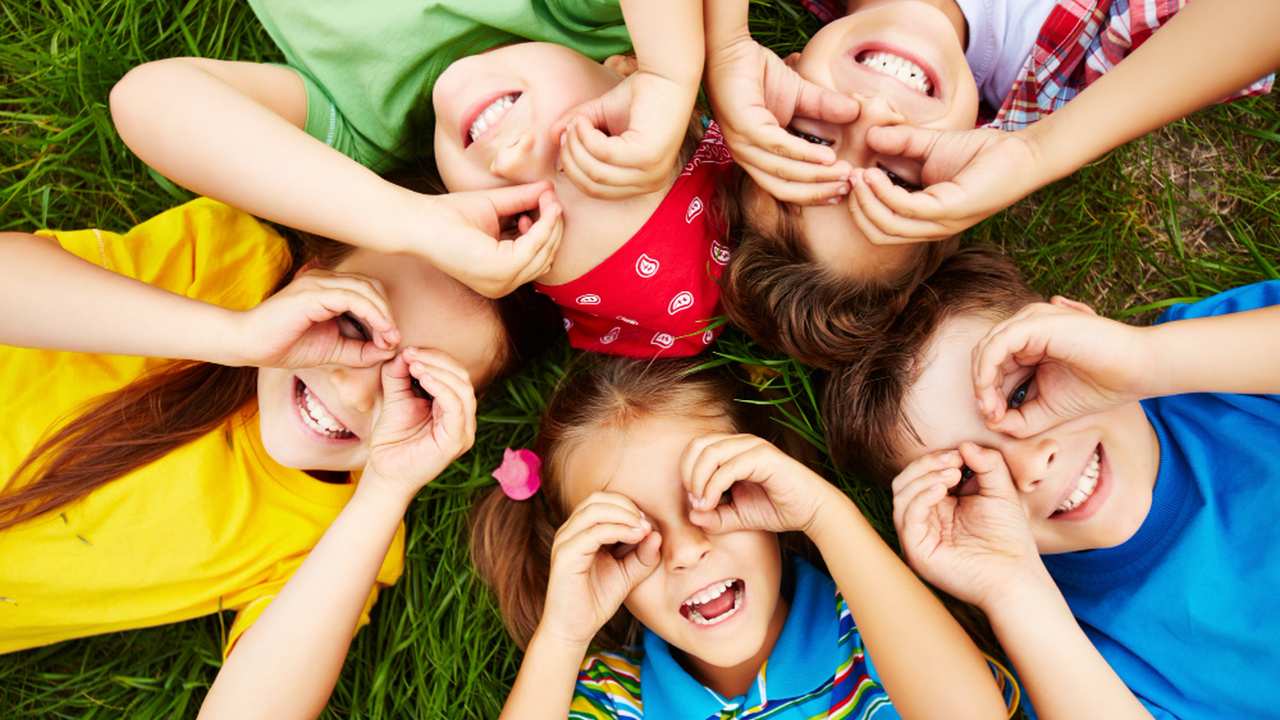 Crianças felizes brincando na grama, com as mãos nos olhos, simbolizando a infância e a inocência.