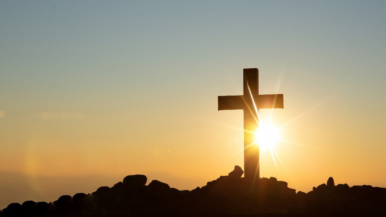 Cruz silhueta contra o sol, simbolizando fé e esperança.