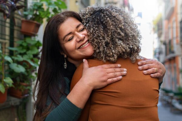 Duas mulheres se abraçam com carinho em uma campanha contra violência de gênero.