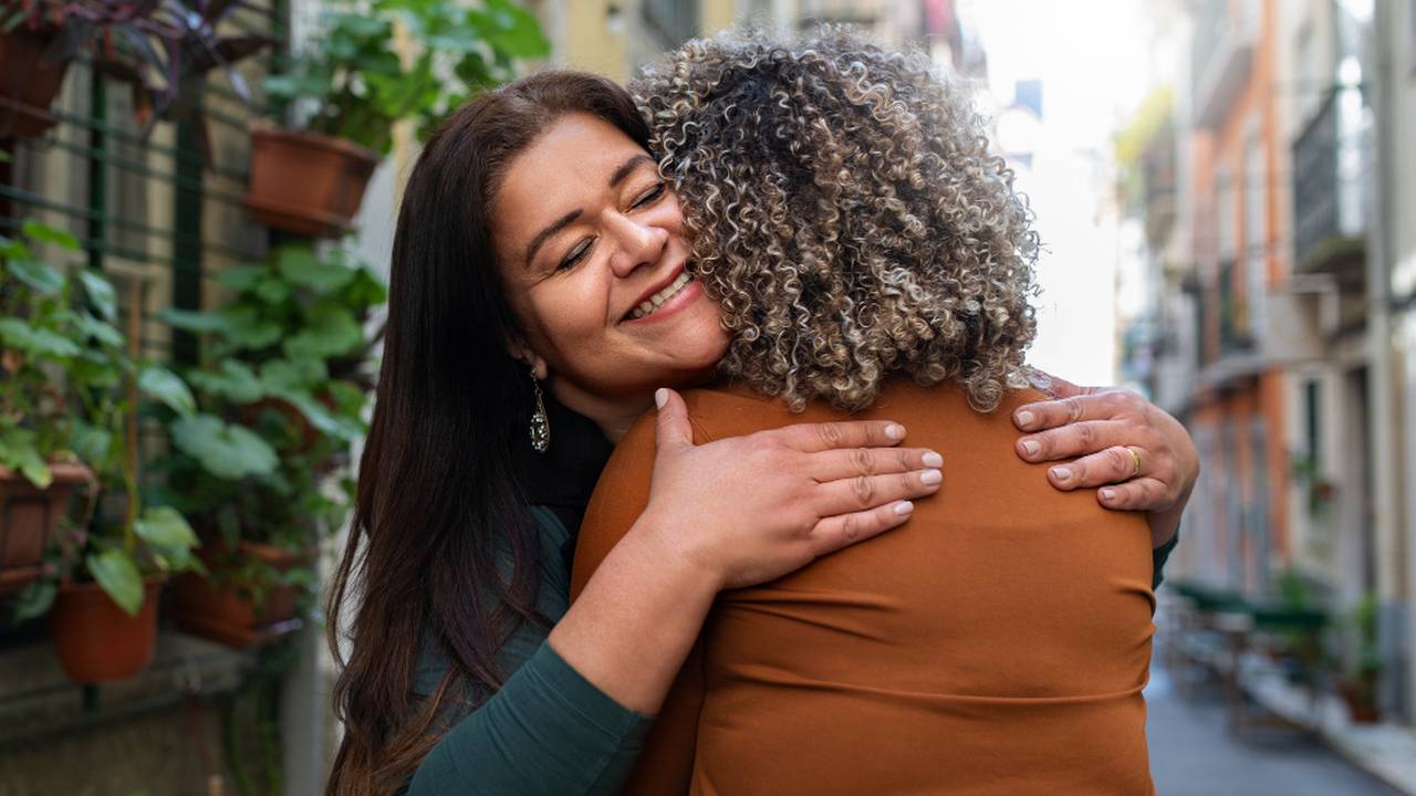 Duas mulheres se abraçam com carinho em uma campanha contra violência de gênero.