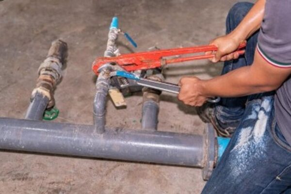 Encanador trabalhando em tubulação de água, possivelmente resolvendo problemas de abastecimento.