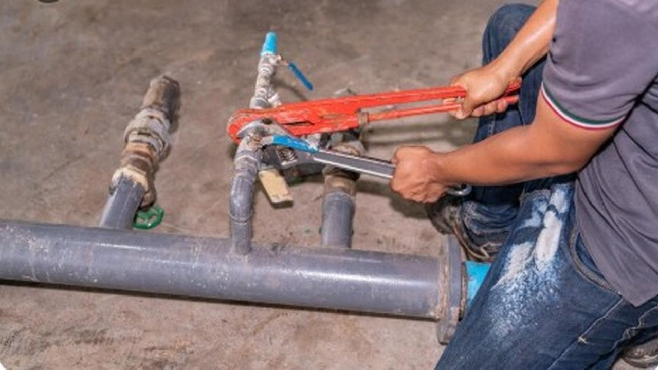 Encanador trabalhando em tubulação de água, possivelmente resolvendo problemas de abastecimento.