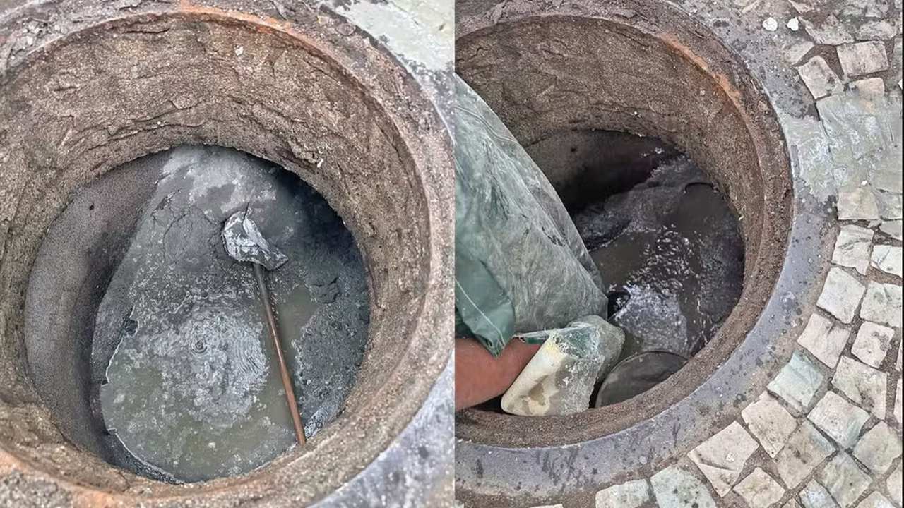 Esgoto entupido: homem inspeciona bueiro com cimento, possível obstrução por concessionária.