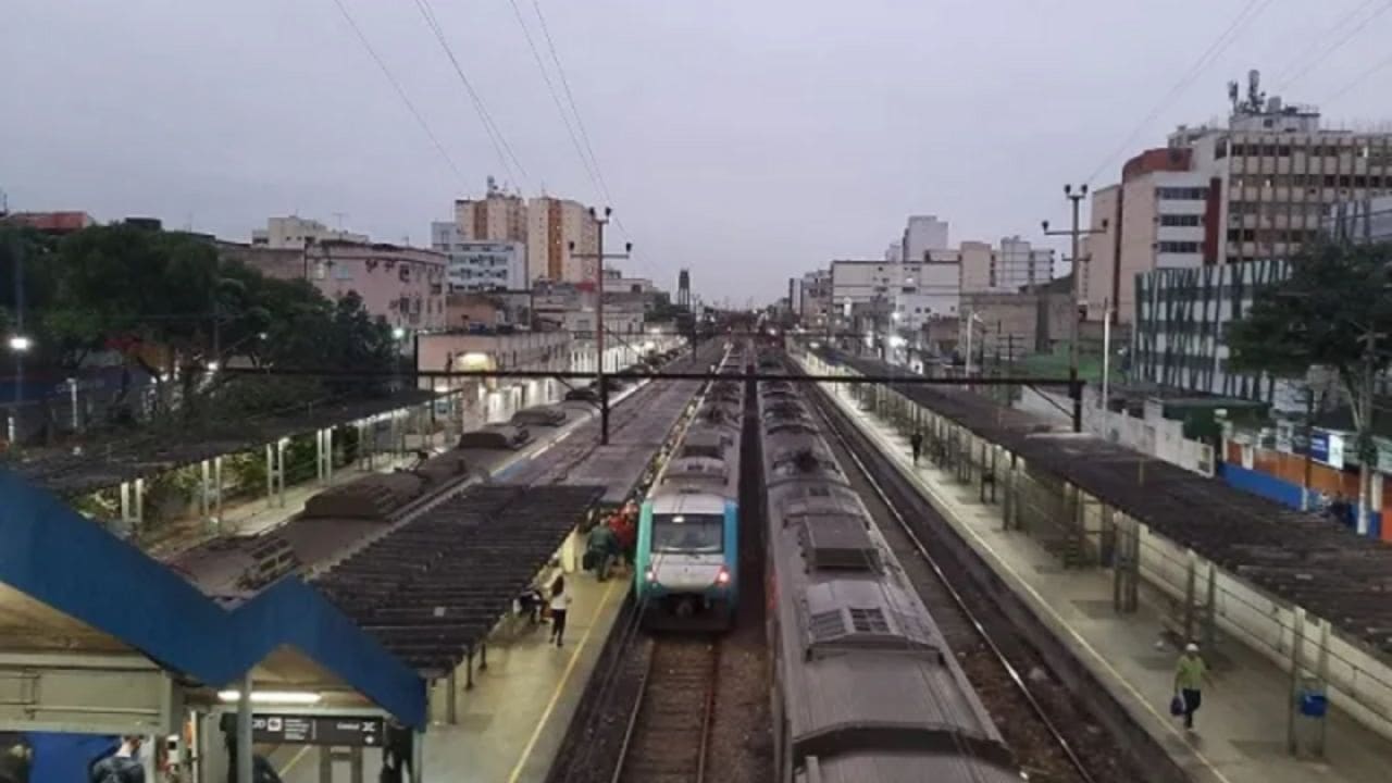 Estação de trem em dia nublado com trens estacionados e prédios ao fundo
