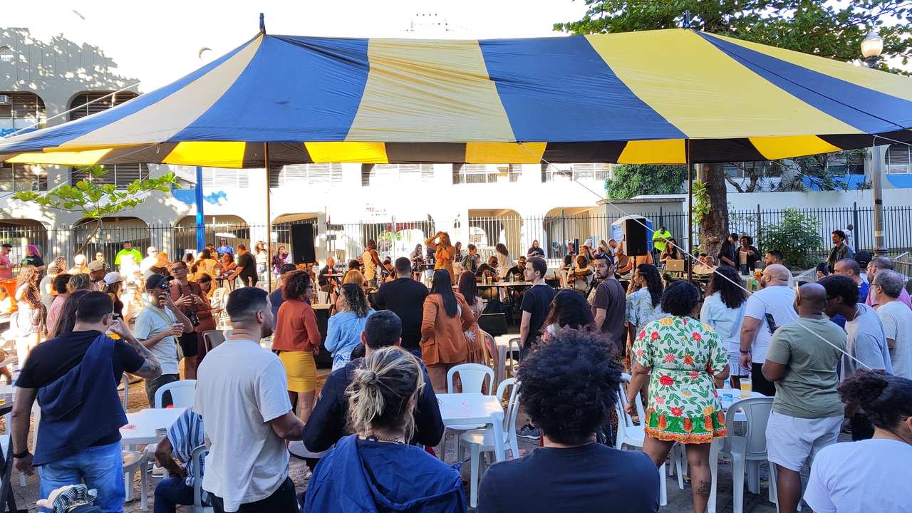 Evento Samba da Feira com roda de samba e público reunido sob tenda colorida.