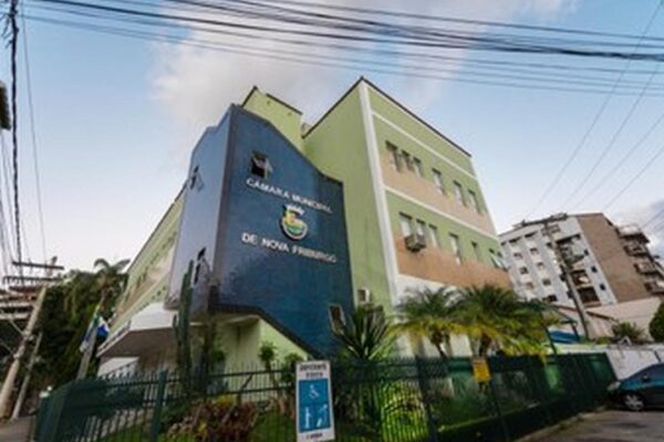 Fachada da Câmara Municipal de Nova Friburgo, Brasil, com céu azul e vegetação ao redor.