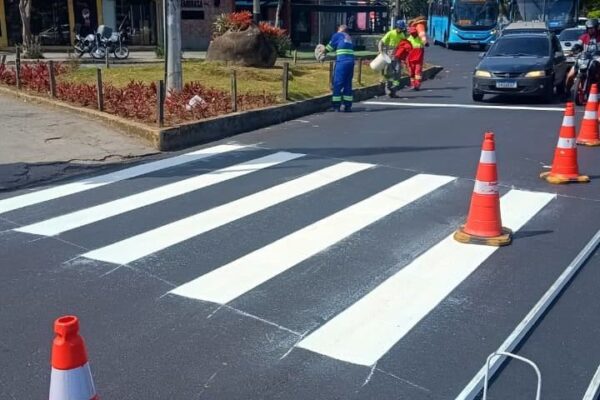 Faixa de pedestres recém-pintada em frente ao Hospital Raul Sertã, com operários trabalhando e cones de sinalização.
