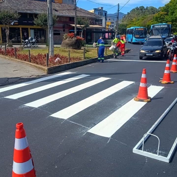 Faixa de pedestres recém-pintada em frente ao Hospital Raul Sertã, com operários trabalhando e cones de sinalização.