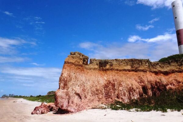 Falésia colorida em São Francisco de Itabapoana, com farol ao fundo e praia.