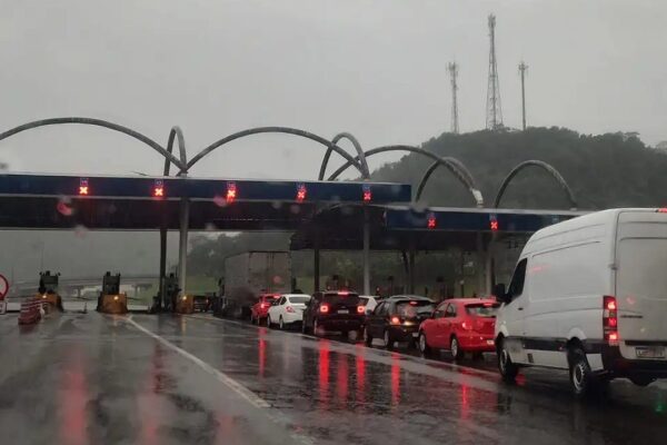 Fila de carros em pedágio na BR-040, com chuva e sinalização