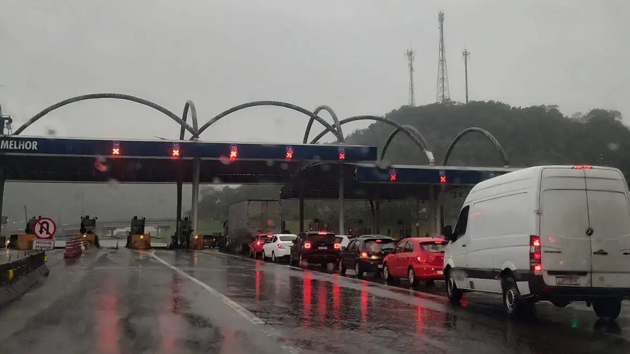 Fila de carros em pedágio na BR-040, com chuva e sinalização