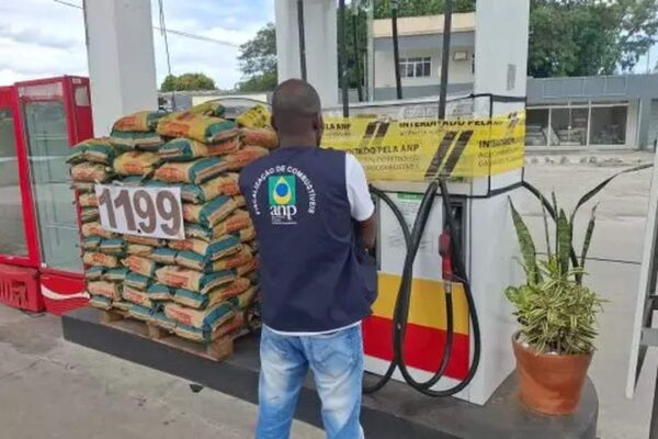 Fiscalização da ANP em posto de combustível, com produtos empilhados e bomba interditada.