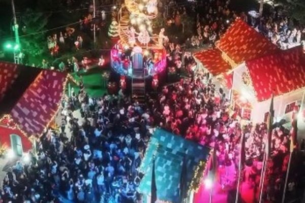 Foto aérea de festa de Natal com multidão, árvores iluminadas e casas decoradas.