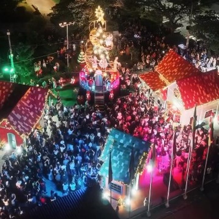 Foto aérea de festa de Natal com multidão, árvores iluminadas e casas decoradas.