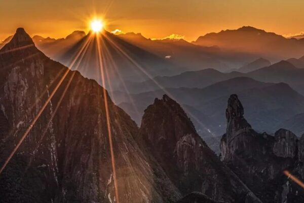 Foto da Serra dos Órgãos, com o icônico Dedo de Deus sob a luz do sol.