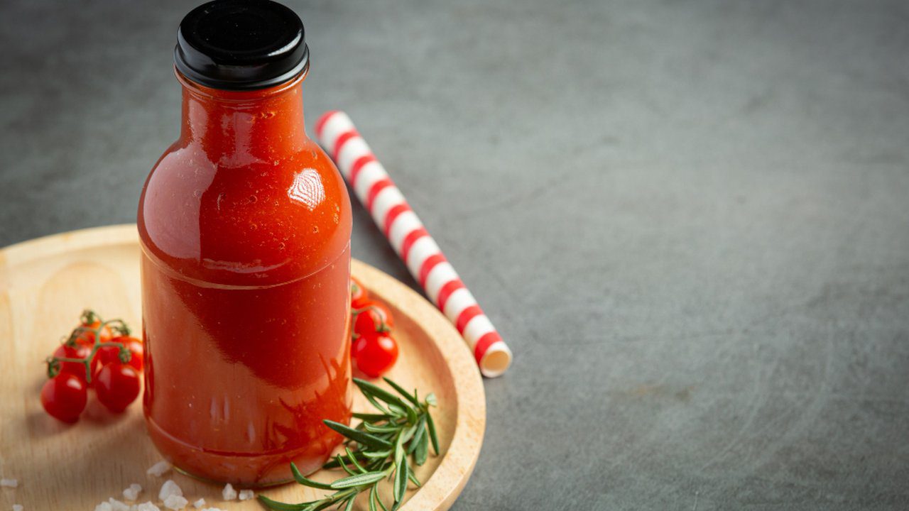 Frasco de molho de tomate com tampa preta em bandeja de madeira, com ingredientes e palito.