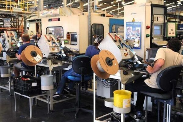 Funcionários trabalhando em fábrica de vestuário, com máquinas e bobinas de fios.