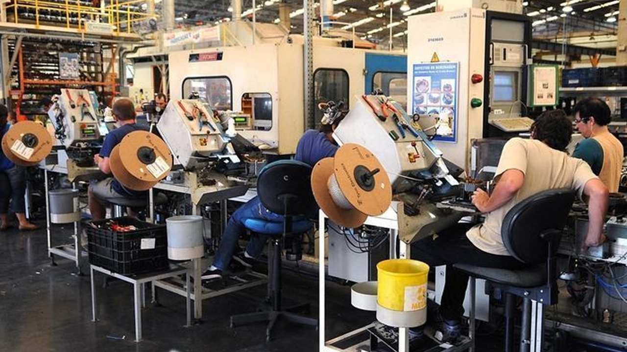 Funcionários trabalhando em fábrica de vestuário, com máquinas e bobinas de fios.