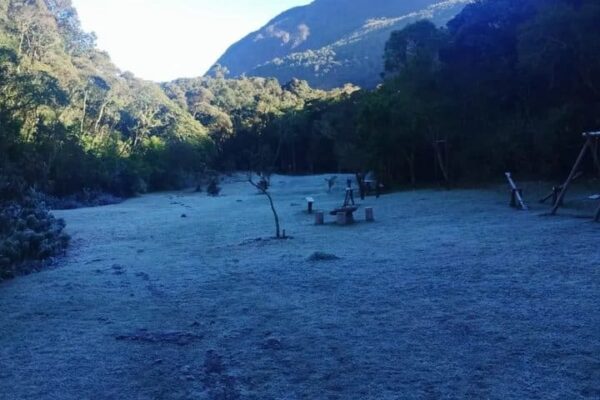 Geada no Parque Estadual dos Três Picos, mostrando gramado coberto e montanhas ao fundo.