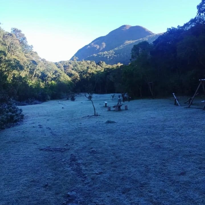 Geada no Parque Estadual dos Três Picos, mostrando gramado coberto e montanhas ao fundo.