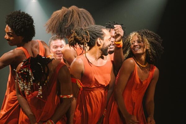 Grupo de dançarinos em trajes laranja se apresenta em evento cultural no Rio de Janeiro.