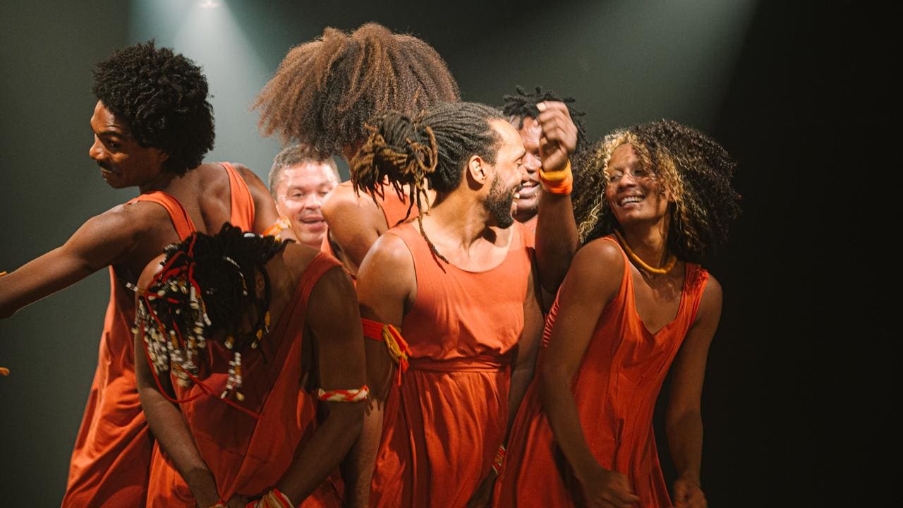 Grupo de dançarinos em trajes laranja se apresenta em evento cultural no Rio de Janeiro.