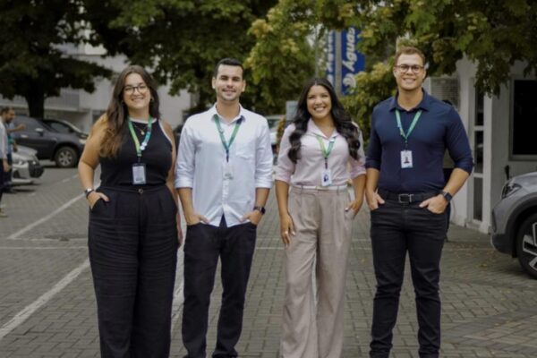 Grupo de jovens profissionais sorrindo e posando para foto em frente a um prédio.