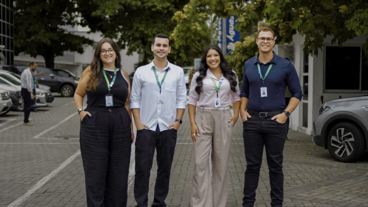 Grupo de jovens profissionais sorrindo e posando para foto em frente a um prédio.