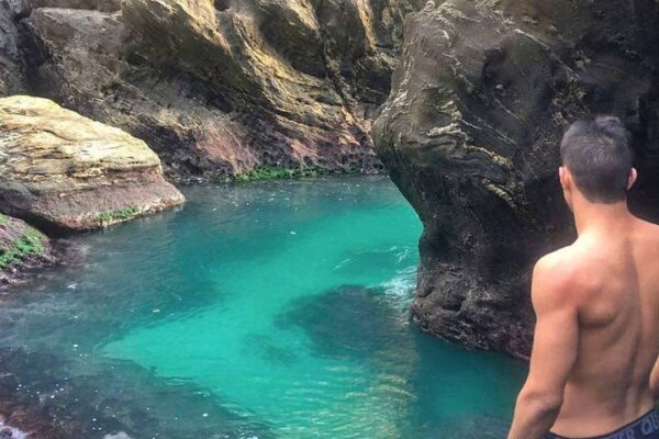 Homem admirando a beleza da Gruta de Ponta Negra em Maricá, com águas cristalinas e rochas.