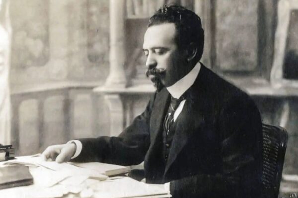 Homem de terno sentado à mesa, provavelmente em um escritório, em imagem em preto e branco.
