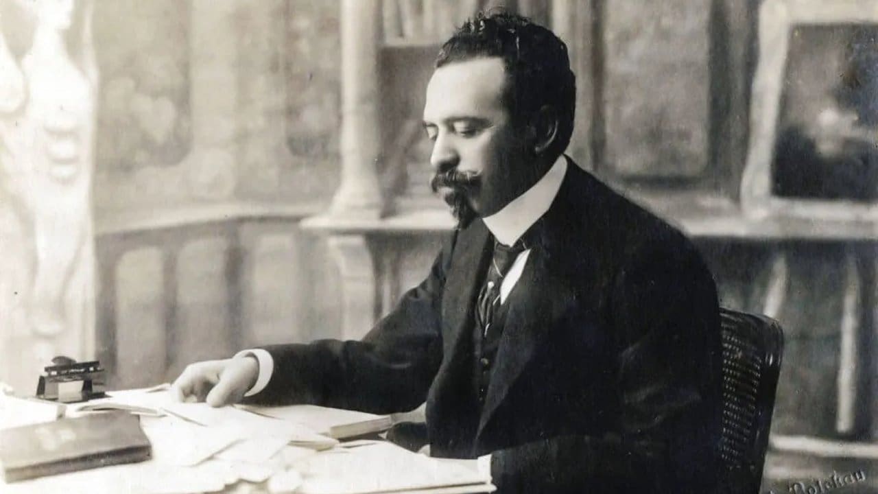 Homem de terno sentado à mesa, provavelmente em um escritório, em imagem em preto e branco.