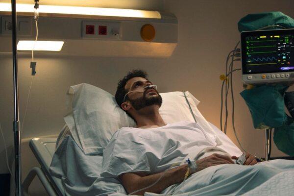 Homem em leito de hospital com máscara de oxigênio, monitor de sinais vitais e soro.