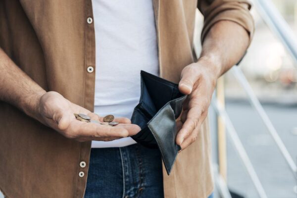 Homem mostrando carteira vazia e algumas moedas na mão, simbolizando dificuldades financeiras.