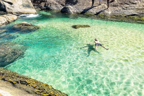 Homem relaxando nas águas cristalinas da Praia do Secreto, Rio de Janeiro.