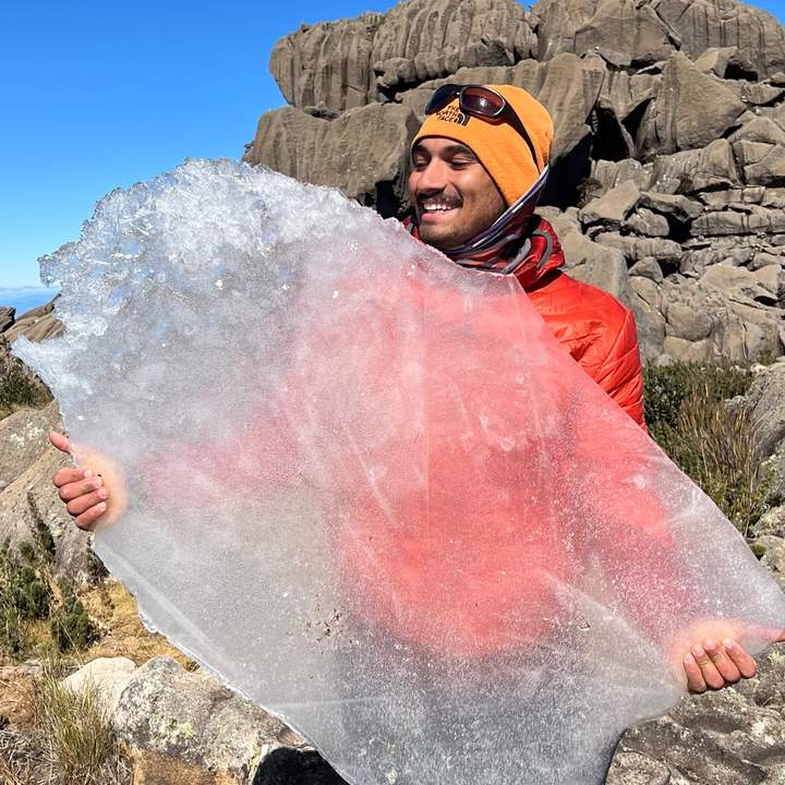 Homem sorrindo segura grande placa de gelo no Parque Nacional do Itatiaia.