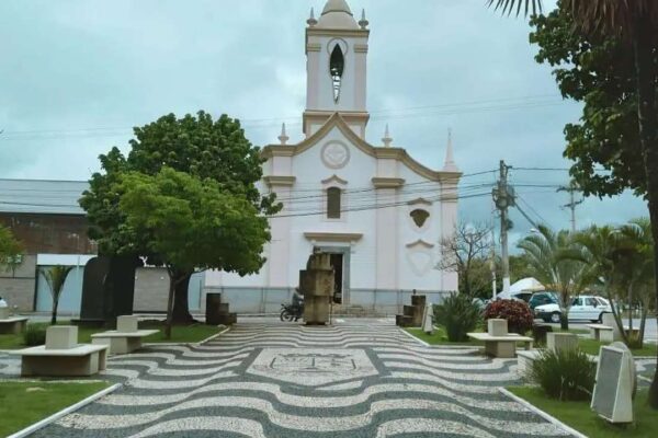 Igreja em Itaocara, Rio de Janeiro, com calçada em padrão ondulado e árvores ao redor.