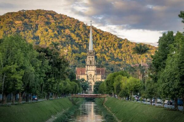 Igreja em Petrópolis em meio à vegetação exuberante, com rio e ponte.