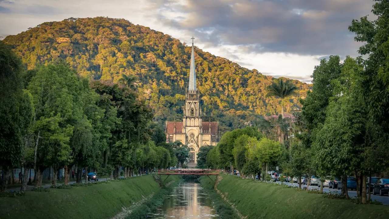 Igreja em Petrópolis em meio à vegetação exuberante, com rio e ponte.
