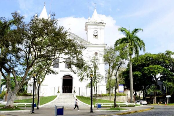 Igreja Matriz de Nossa Senhora da Conceição, com arquitetura em branco, árvores e céu azul.