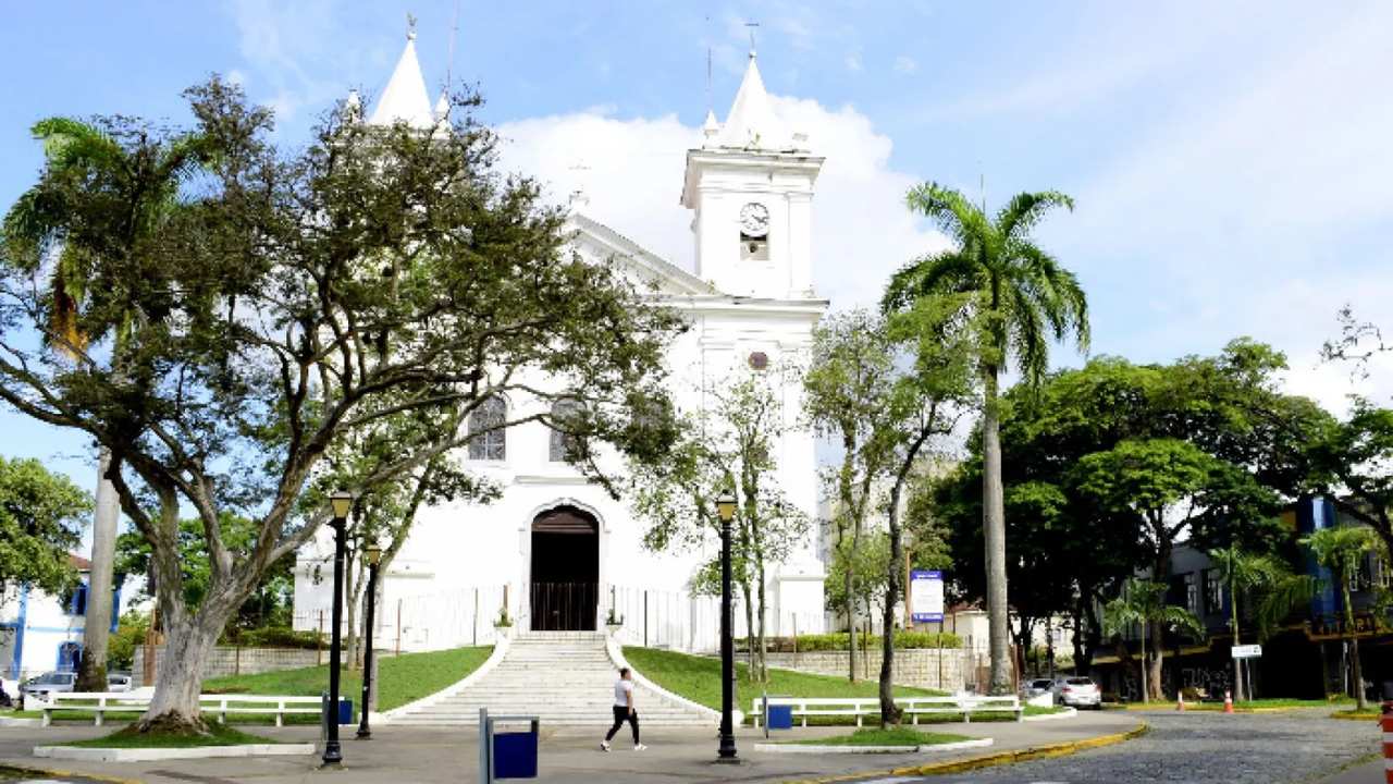 Igreja Matriz de Nossa Senhora da Conceição, com arquitetura em branco, árvores e céu azul.