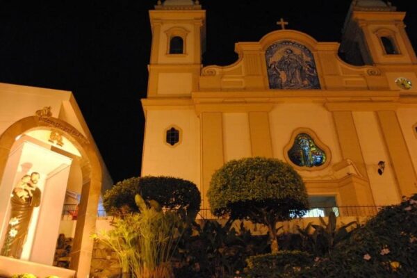 Igreja Matriz de São José de Avaí iluminada à noite, com estátua em primeiro plano.