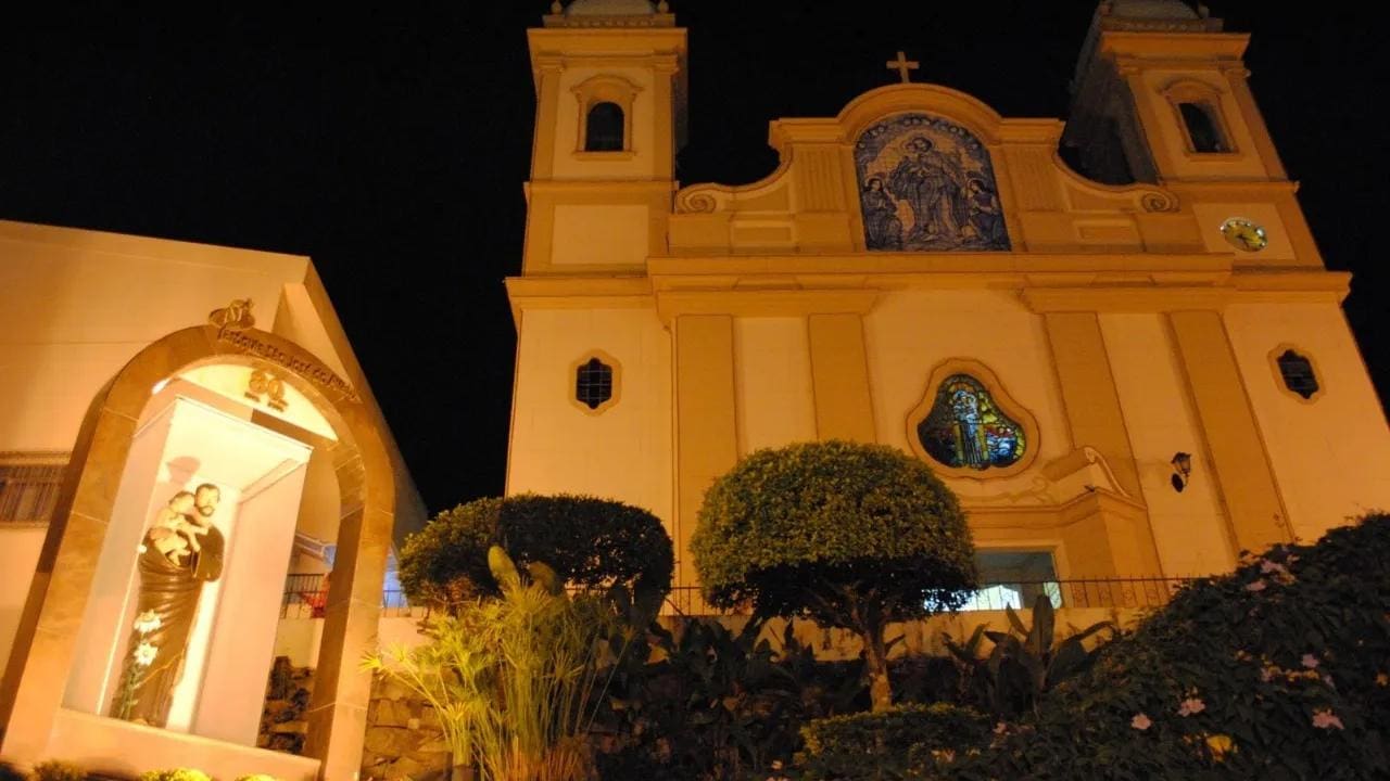 Igreja Matriz de São José de Avaí iluminada à noite, com estátua em primeiro plano.