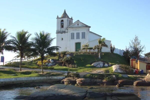 Igreja São João Batista em Casimiro de Abreu, com vista para o mar e palmeiras.
