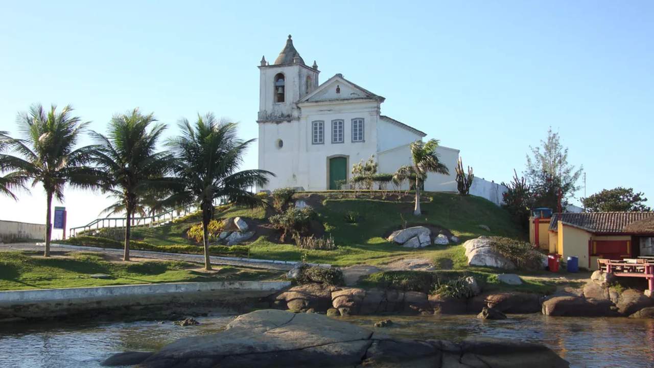 Igreja São João Batista em Casimiro de Abreu, com vista para o mar e palmeiras.