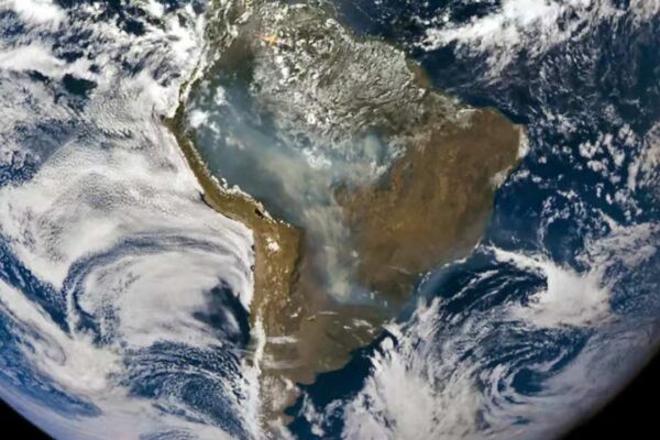 Imagem de satélite mostrando a América do Sul, com nuvens e uma grande quantidade de fumaça sobre o continente.