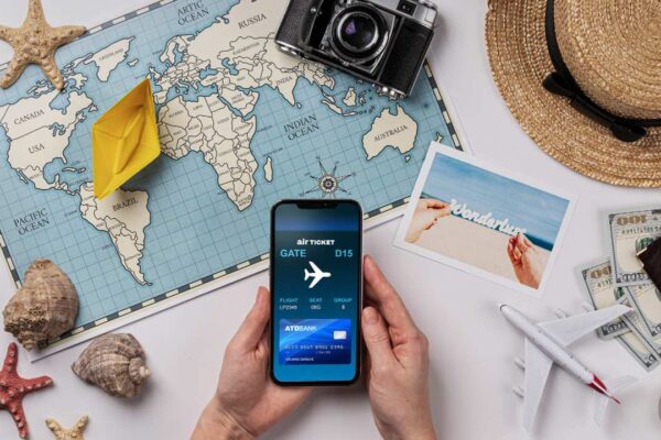 Imagem de viagem com mapa, celular com passagem aérea e outros objetos turísticos.