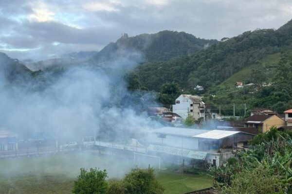 Incêndio na sede do Lumiar Futebol Clube em Nova Friburgo, com fumaça densa e montanhas ao fundo.